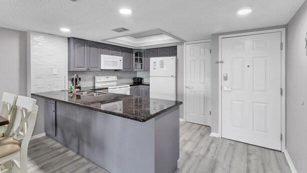 A modern kitchen with grey cabinets, a granite island, white appliances, and a white door. - Sandy Shores 311 Water View 2 BR (Madeira Beach)
