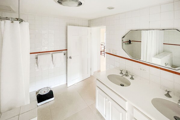 A bathroom with white tiles, a large mirror, two sinks, and a shower area. - Coral Sea Oasis with private beach and infinity Pool (Hamilton)