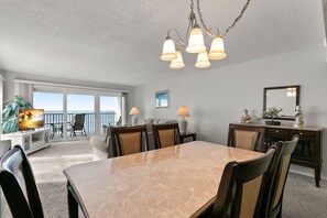 Un espace repas avec une table et des chaises en marbre, un lustre et une vue sur l’océan grâce à de grandes fenêtres.