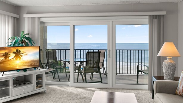 Une chambre d’hôtel avec un balcon donnant sur l’océan, une télévision, un canapé et une lampe.