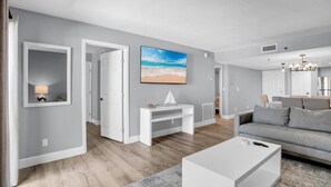 Un salon moderne avec un canapé gris, une table basse blanche et un tableau représentant une scène de plage.