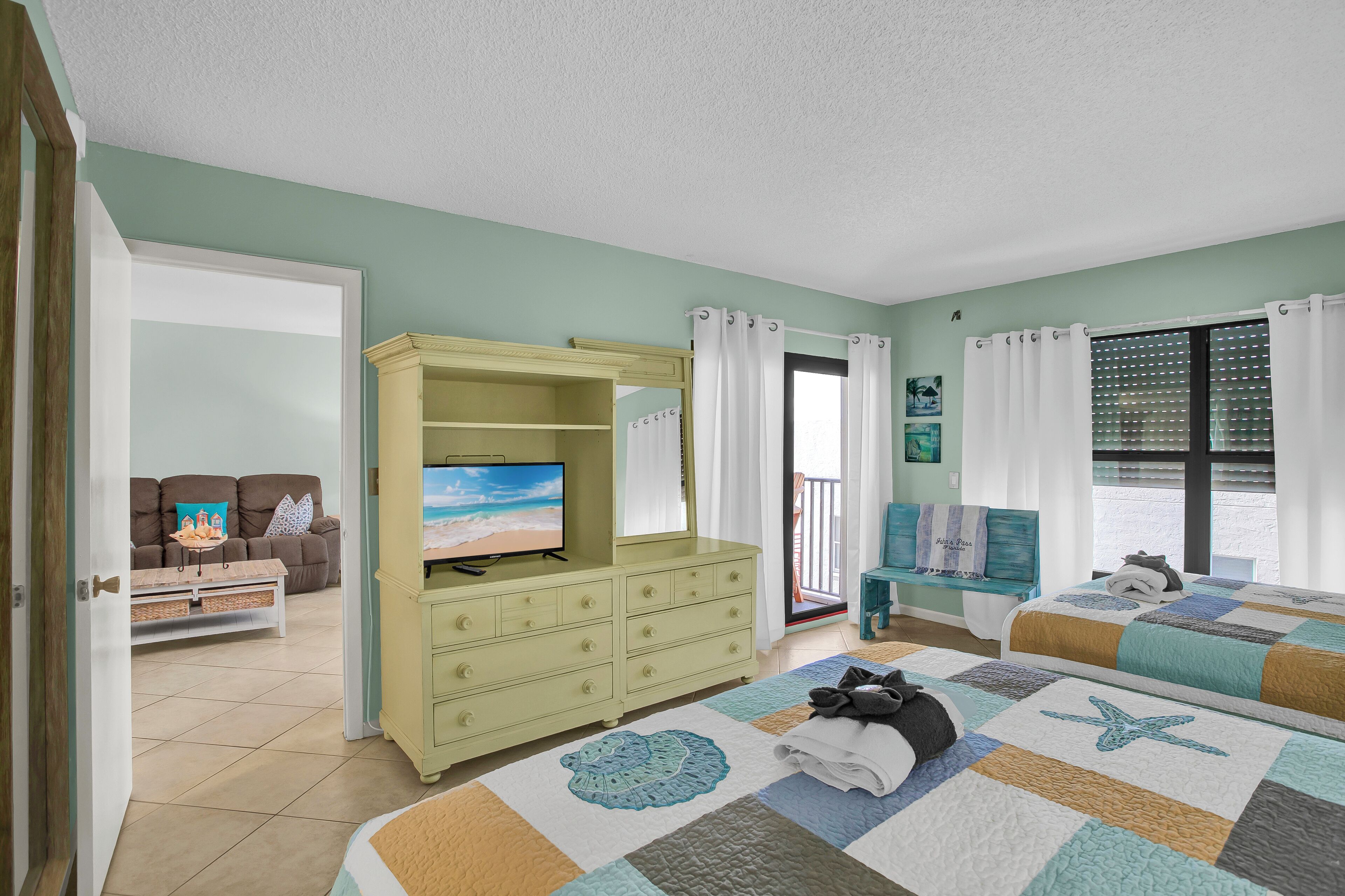 A bedroom with two beds, a TV, a dresser, and a balcony with a view.