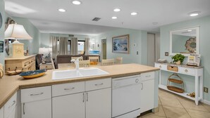 A kitchen with white cabinets, a sink, and a countertop. There is a dining area with a table and chairs.