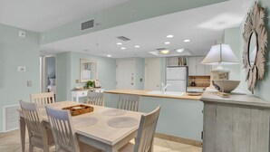 A dining area with a wooden table and chairs, a kitchen with white cabinets, and a decorative mirror on the wall.