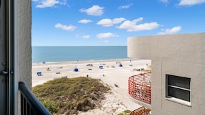 A beach view from a balcony with a clear sky, sandy beach, and a few people.