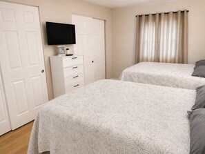 Un dormitorio con dos camas, un televisor sobre un tocador y una puerta con cortina.
