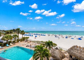 Una playa con piscina, palmeras y sombrillas de paja.