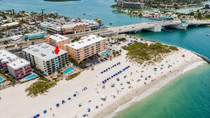 Un hotel frente al mar con varias construcciones, una playa con sombrillas y un puerto deportivo con barcos.