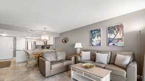 A modern living room with a beige sofa, a coffee table, and a dining area with a wicker table and chairs.