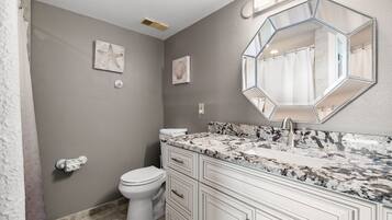 Un baño con inodoro blanco, tocador de mármol y un espejo hexagonal grande.