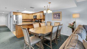 Una cocina moderna con armarios de madera, un refrigerador de acero inoxidable y una zona de comedor con mesa y sillas de madera.