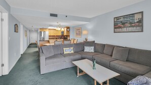Una sala de estar con un sofá seccional gris, una mesita blanca y una lámpara verde.