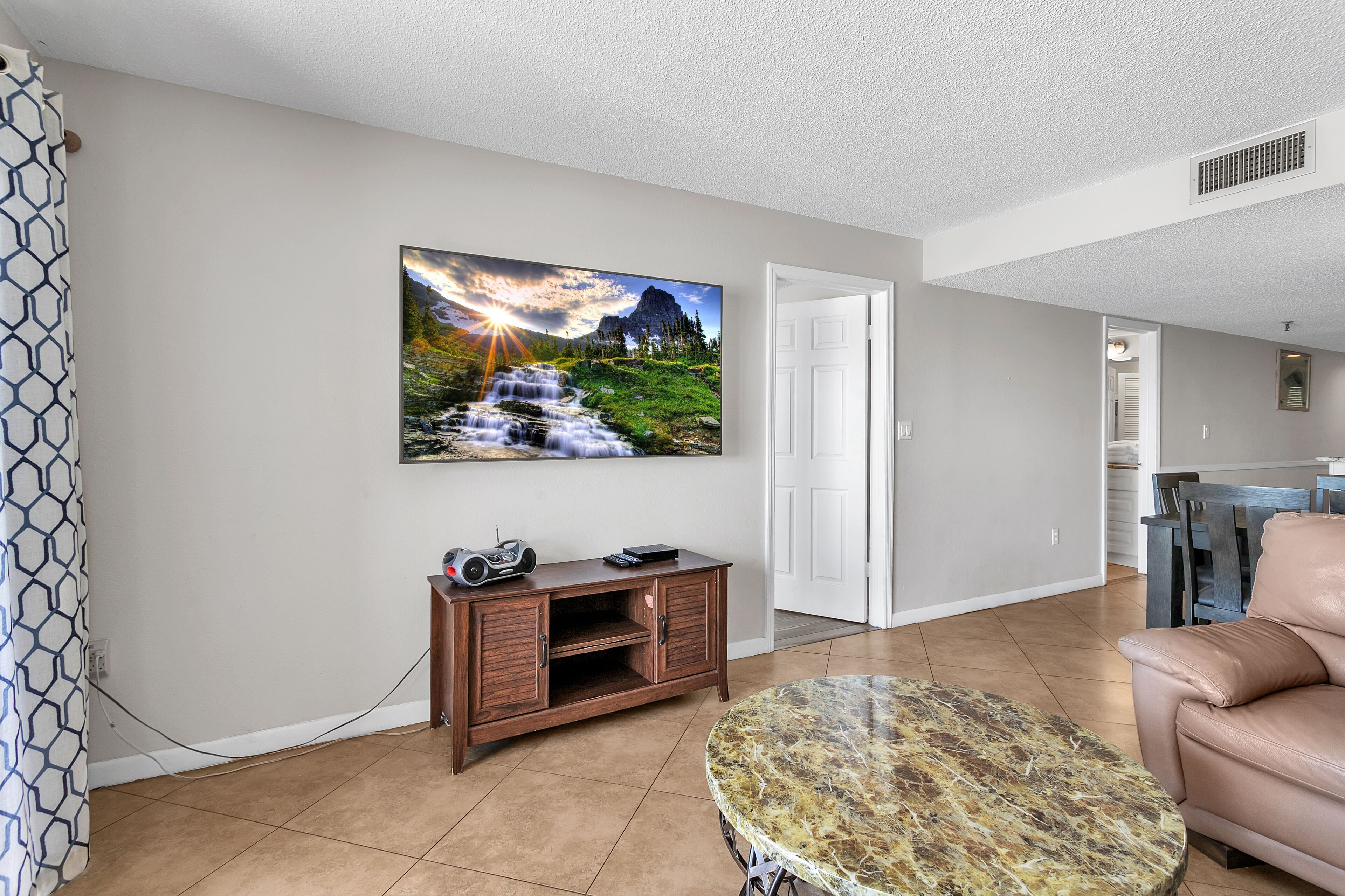 A living room with a large painting of a waterfall, a wooden cabinet, a round coffee table, and a beige sofa.