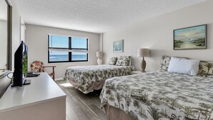 Une chambre d’hôtel avec deux lits, un bureau avec un ordinateur, une chaise et une fenêtre donnant sur l’océan.