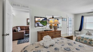 Una habitación de hotel con cama, sofá, televisor, cómoda y ventana con persianas.