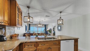 Una cocina con armarios de madera, encimera de granito, lavavajillas y luces colgantes.