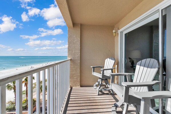 Un balcón con vista a la playa, dos sillas Adirondack y una mesa.