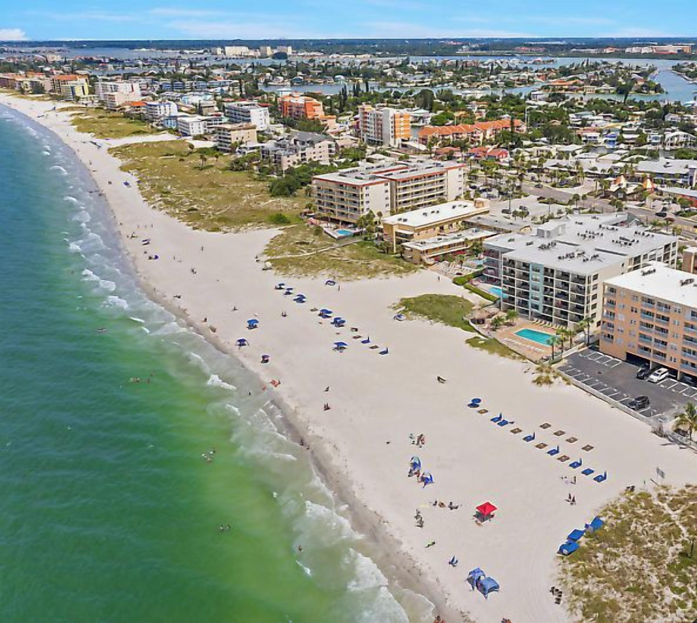 An aerial view of a coastal hotel with a beach, multiple buildings, and a pool area.