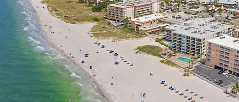An aerial view of a coastal hotel with a beach, multiple buildings, and a pool area.