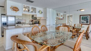 A modern kitchen with white cabinetry, a glass island, and wicker chairs.