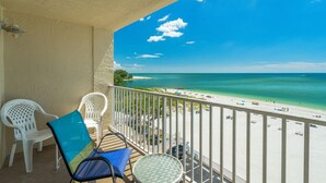 A balcony with a view of a beach, white chairs, and a table.