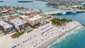 An aerial view of a coastal city with a beach, a bridge, and a hotel with multiple floors and balconies. - Get Away In This Well-Appointed Gulf Front Condo (Madeira Beach)