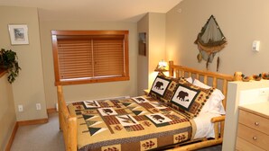 A bedroom with a wooden bed, a window with blinds, a wall-mounted fish net, and a bedside lamp. - Bear Creek Crossing - Your Cabin In A Condo! (Alberta)