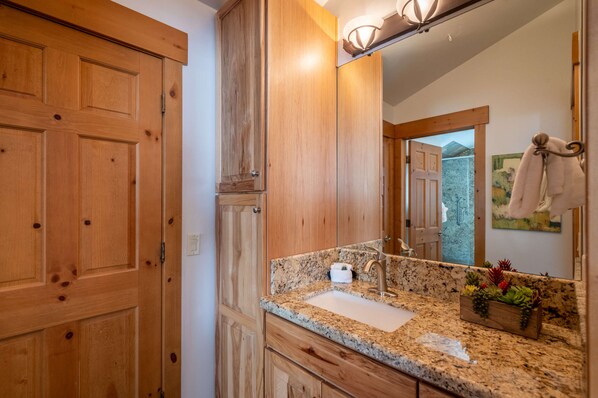 A bathroom with wooden cabinets, a granite countertop, a sink, and a mirror.