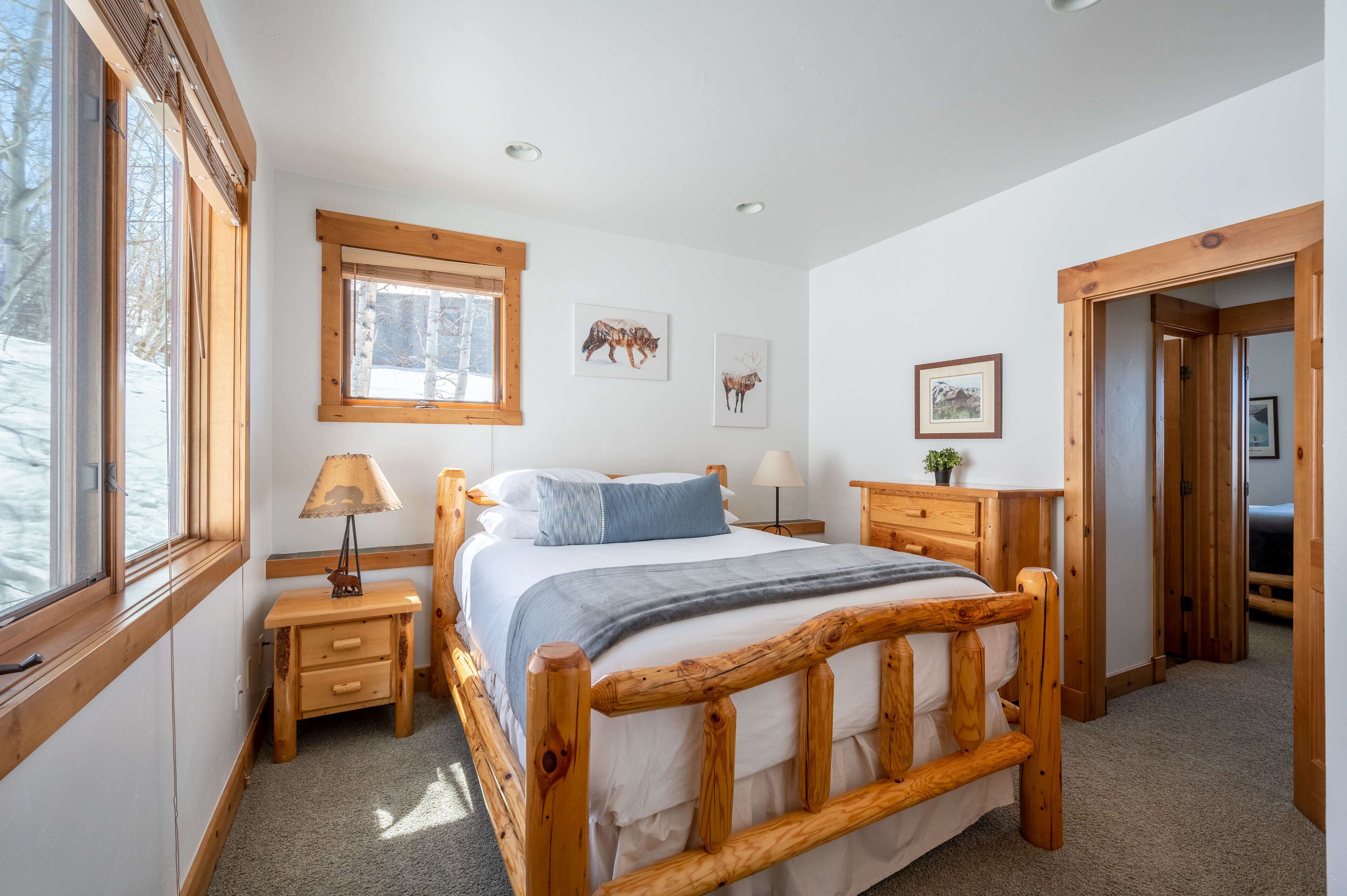 A wooden bed with a headboard, a bedside table with a lamp, and a window with blinds.