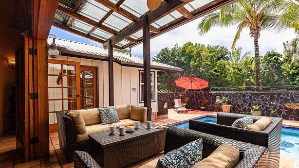 A covered outdoor seating area with wicker furniture, a pool, and a stone wall. - House of Paddles, POOL, Ocean close in Keaau, Hawaii, near Hilo (Keaau)