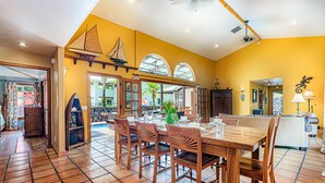 A dining area with a wooden table and chairs, a sailboat decoration, and a view of the outside. - House of Paddles, POOL, Ocean close in Keaau, Hawaii, near Hilo (Keaau)