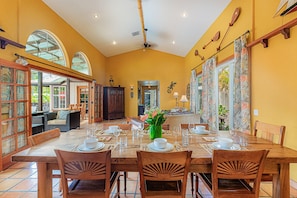 A dining area with a large wooden table set for six, surrounded by wooden chairs.