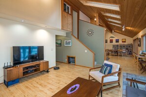 Relax in a spacious living area with a high ceiling, featuring a flat-screen TV, soundbar, and gaming console.