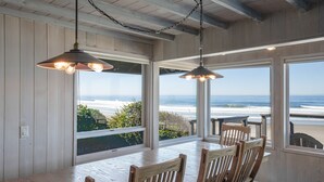 A dining area with wooden furniture and large windows overlooking the beach. - Enjoy the waves in the hot tub at this beachfront home with direct beach access (Lincoln city)