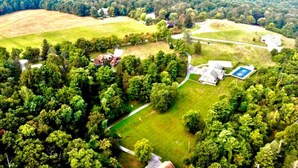 An aerial view of a property with multiple buildings, a large green field, and dense forested areas. - Scenic Mountaintop Villa with Free WiFi & Pool (Waynesboro)