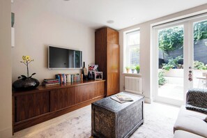 Ein modernes Wohnzimmer mit einer Holzeinbauwand, einem Flachbildfernseher, einem Couchtisch und Blick auf den Garten durch eine Glastür.