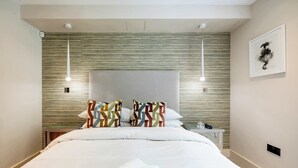 A neatly made bed with a patterned blanket, a headboard with a textured design, and a framed artwork on the wall.