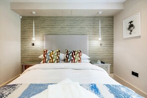 A neatly made bed with a patterned blanket, a headboard with a textured design, and a framed artwork on the wall.