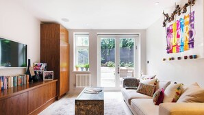 A modern living room with a large TV, wooden cabinet, and a colorful wall art piece.