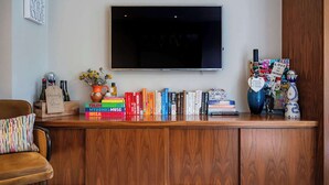 A living room with a flat-screen TV mounted on the wall, a wooden entertainment unit with books and decorative items, a sofa, and a coffee table.