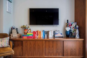 A living room with a flat-screen TV mounted on the wall, a wooden entertainment unit with books and decorative items, a sofa, and a coffee table.