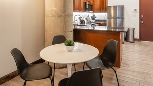 Une cuisine moderne avec des meubles en bois, des appareils électroménagers en acier inoxydable et une table de salle à manger ronde, assortie de chaises noires.