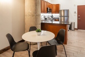 Une cuisine moderne avec des meubles en bois, des appareils électroménagers en acier inoxydable et une table de salle à manger ronde, assortie de chaises noires.