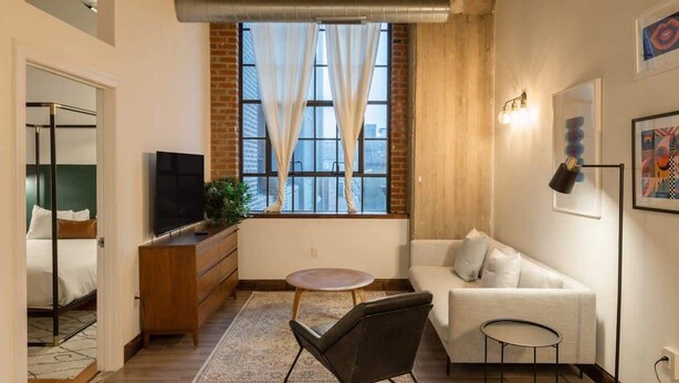 Un espace de vie compact comprenant un canapé, un téléviseur, une petite table et une fenêtre avec des rideaux.