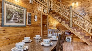 A wooden cabin interior with a dining area, a staircase, and framed pictures on the walls. - 4 Bedrooms Near Pigeon Forge-Hot Tub-Pet Friendly-Sleeps 12 (Sevierville)