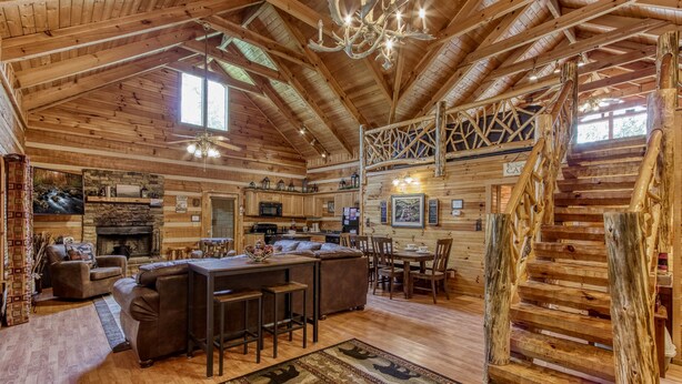 A rustic cabin interior with a wooden ceiling, a fireplace, a dining area, and a staircase. - 4 Bedrooms Near Pigeon Forge-Hot Tub-Pet Friendly-Sleeps 12 (Sevierville)