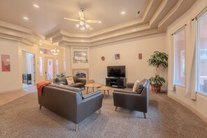 A spacious living room with a flat-screen TV, two leather sofas, a coffee table, and a ceiling fan.