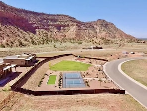 Un complexe sportif comprenant un court de tennis, un terrain de basketball et un espace clos avec un terrain gazonné.