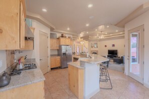 A spacious kitchen with a central island, a dining area, and a living room with a TV.