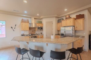Uma cozinha moderna com ilha central, banquetas, eletrodomésticos de aço inoxidável e armários de madeira.